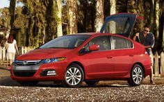 a red car with its hood open and people looking at it in front of some trees