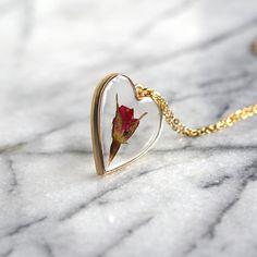 A single rose for the perfect gift for the unique gal in your life. A rose is encased in jewelry grade resin, within an antique bronze or gold plated heart bezel. The bezel is 1 1/2 inches in length and 1 1/4 inches in width- the matching chain is 24 inches. Chain is finished with a lobster clasp. Necklace will arrive attached to card shown in photos. Ready to be gifted! This necklace is custom made. Just like nature, no two will be exactly alike! Let me assure you, though, that we replicate eac Rose Jewelry For Valentine's Day, Rose-colored Heart-shaped Jewelry For Gifts, Rose Heart-shaped Jewelry Gift, Rose Heart-shaped Necklace For Gift, Rose Heart-shaped Jewelry For Gift, Heart-shaped Rose Colored Jewelry For Gift, Heart-shaped Rose Jewelry For Gift, Valentine's Day Rose Jewelry Gift, Valentine's Day Gift Jewelry With Rose Design