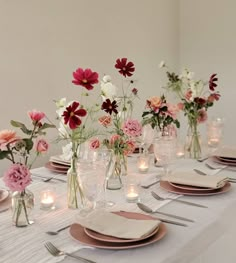 a table set with plates and vases filled with pink, white and red flowers