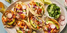 several tacos on a paper plate with limes and other food items around them