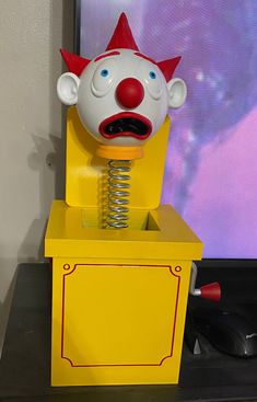 a yellow box with a clown head on top of it and a mouse in the bottom