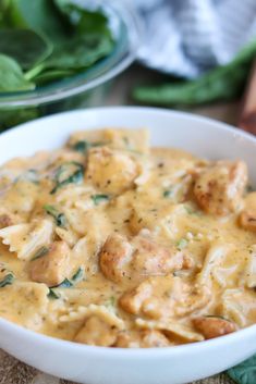 a white bowl filled with pasta and meat covered in gravy next to spinach leaves