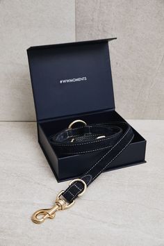 the black leather dog leash with gold hardware is in its box and it has a golden metal