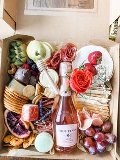 a wine bottle sitting in a box filled with fruit and crackers on top of a table