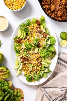 a white plate topped with lettuce and corn next to bowls of sauces