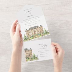 two hands holding up wedding cards with watercolor drawings on them and the same design