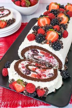 a cake roll with berries and chocolate filling on a black platter next to white plates