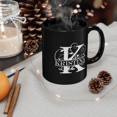 a black coffee mug sitting on top of a table next to candles and pine cones