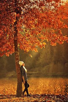 a woman standing next to a tree in the fall