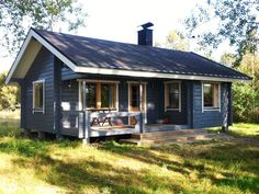 a small blue cabin in the woods with picnic table and chairs on the front porch