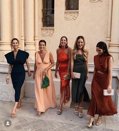 four women in dresses are posing for the camera outside an old building with stone pillars