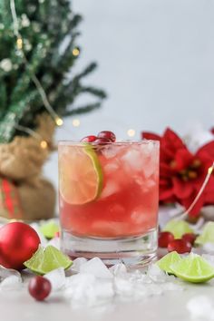 a drink with lime and cranberries in a glass surrounded by christmas decorations on the table