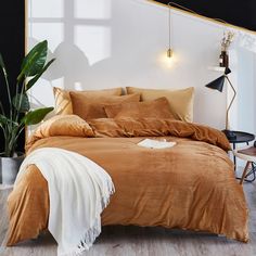 a bed with brown sheets and pillows in a room next to a potted plant