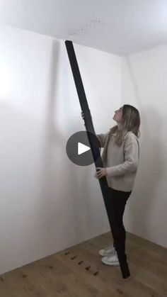 a woman standing on top of a wooden floor next to a black pole in a room