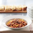 a white bowl filled with pasta and meat on top of a wooden cutting board next to bowls