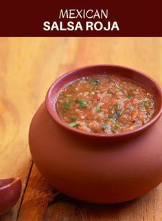 a red bowl filled with soup next to a spoon on a wooden table, ready to be eaten