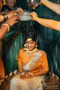 a woman is getting her hair washed by two women in yellow sari and gold jewelry