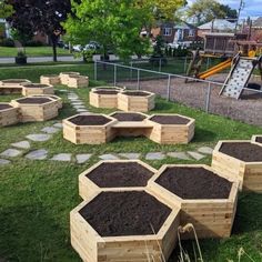 several wooden boxes filled with dirt on top of a grass covered park area next to a playground