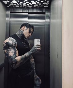 a man with tattoos taking a selfie in an elevator