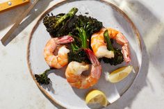 a plate with shrimp, broccoli and lemon wedges next to a knife