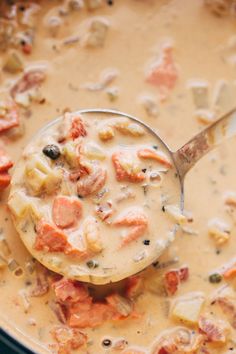 a ladle full of soup with meats and vegetables in it, ready to be eaten