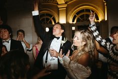 a man in a tuxedo standing next to a woman with her arms up