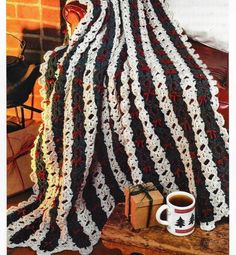 a crocheted blanket sitting on top of a bed next to a cup of coffee