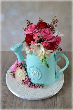 a blue watering can filled with flowers on top of a white plate and saucer