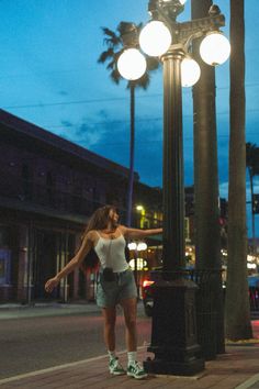 a woman standing next to a lamp post on the side of a road at night