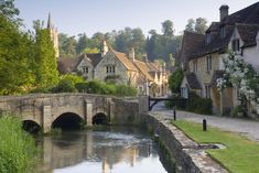 an old stone bridge over a small river in the middle of a village with houses on either side