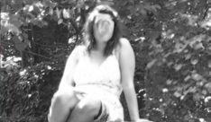 black and white photograph of a woman sitting on a bench in front of some trees