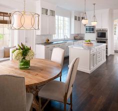 a kitchen and dining room with white cabinets, wood floors and an island in the middle