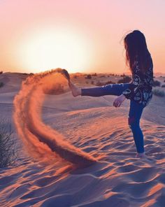 a woman throwing sand into the air on top of a sandy dune at sunset or dawn