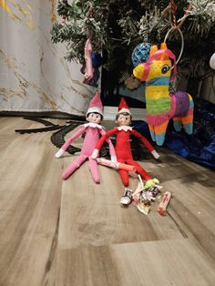 two elf dolls laying on the floor next to a christmas tree and stuffed toy horse