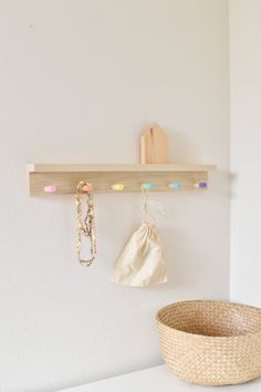 a white wall with a wooden shelf and some necklaces on it next to a basket