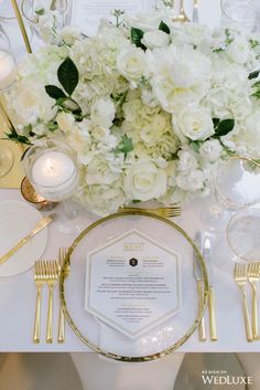 a table setting with white flowers and gold place settings