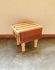 a small wooden stool sitting on top of a floor next to a wall with a pattern