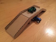 an open cardboard box on the floor with a toy tractor and ramp made out of it