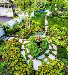 a garden with lots of green plants and stepping stones in the center, surrounded by greenery