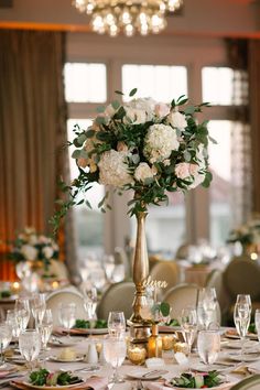 a tall vase filled with flowers on top of a table covered in white linens