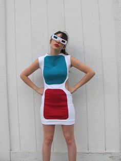 a woman standing in front of a white wall wearing a dress with red and blue squares on it