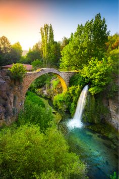 a bridge over a river with a waterfall in the foreground and trees on either side