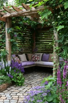 an outdoor seating area with purple flowers and greenery on either side, surrounded by brick pavers