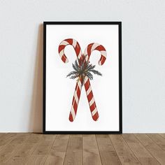 a christmas candy cane is displayed in a frame on a wooden table next to a white wall