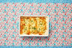 a casserole dish with cheese and herbs on a colorful tablecloth, viewed from above