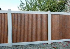 a white fence with wood slats on it and flowers in the gravel behind it