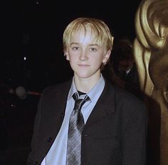 a young man in a suit and tie standing next to an oscar statue at night