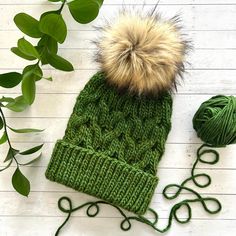 a green knitted hat with a pom - pom sitting next to it