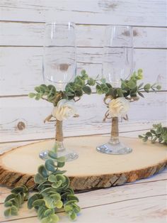 three wine glasses with flowers and greenery in them on a wood slice, ready to be used as centerpieces