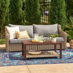 a couch and coffee table on a rug in the middle of a patio with trees